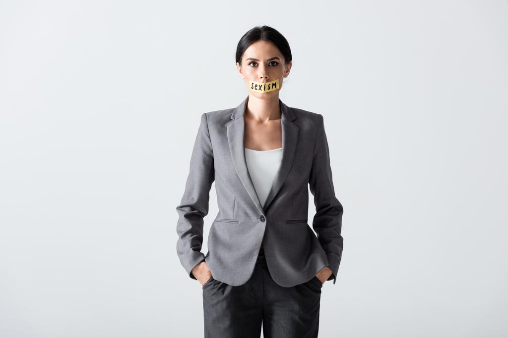 businesswoman with sexism lettering on scotch tape standing with hands in pockets isolated on white  - Photo, Image