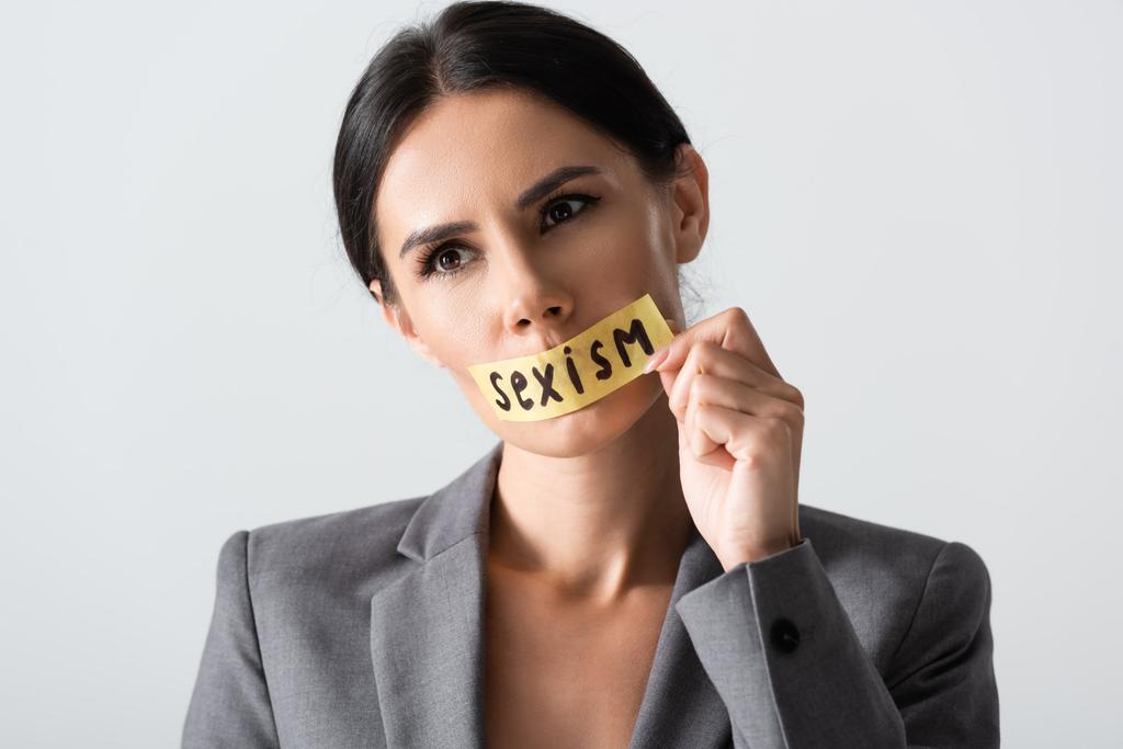 mujer de negocios tocando cinta adhesiva con letras de sexismo en la boca aislado en blanco
 - Foto, imagen