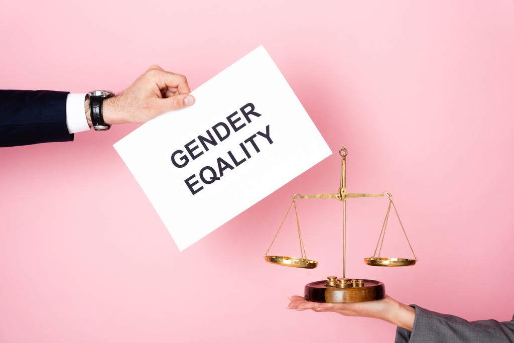 oříznutý pohled na obchodníka držícího plakát s písmeny rovnosti pohlaví v blízkosti podnikatelky se zlatými měřítky na růžové, koncepce rovnosti pohlaví  - Fotografie, Obrázek
