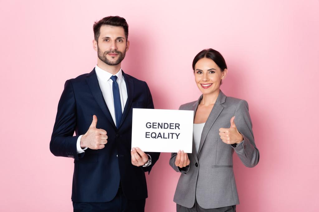 knappe zakenman en zakenvrouw houden bordje met gendergelijkheid belettering en tonen duimen omhoog op roze  - Foto, afbeelding