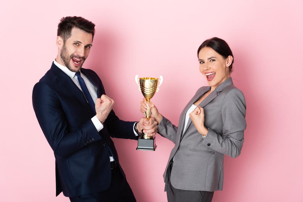 podekscytowany biznesmen i businesswoman w garniturach posiadających trofeum i gestykulując na różowej koncepcji równości płci - Zdjęcie, obraz