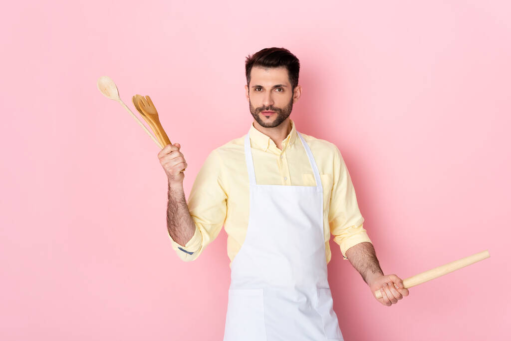 barbudo hombre en delantal sosteniendo rodillo de madera y cuchara en rosa
  - Foto, imagen