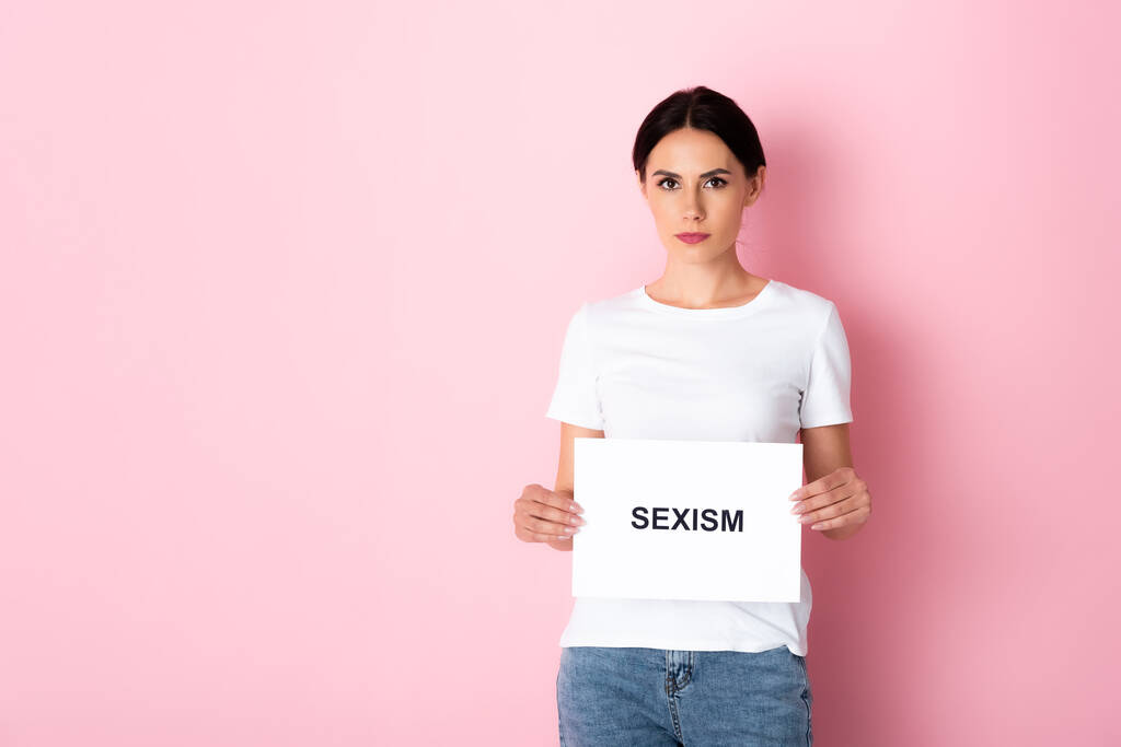 ελκυστική γυναίκα σε λευκό t-shirt κρατώντας πλακάτ με σεξισμό γράμματα σε ροζ  - Φωτογραφία, εικόνα