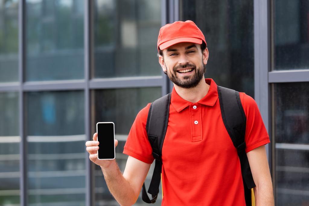 Handsome courier in uniform holding smartphone with blank screen on urban street  - Photo, Image