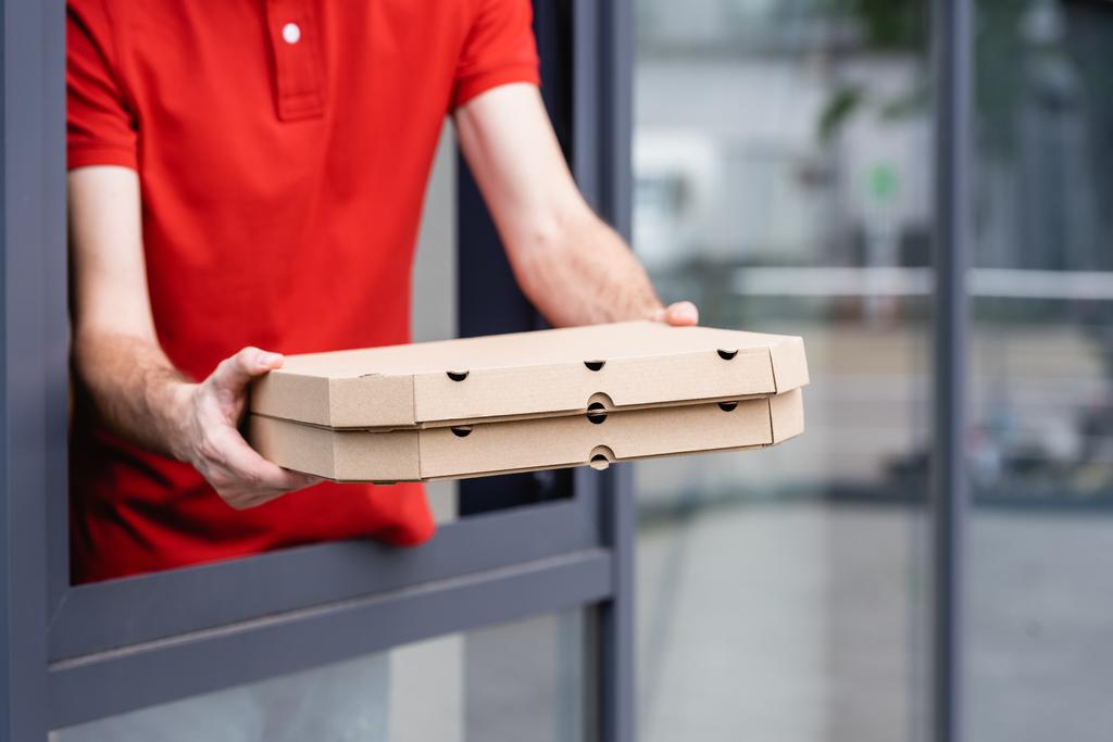 Vue recadrée du serveur tenant pizza à emporter près de la fenêtre du café sur la rue urbaine  - Photo, image
