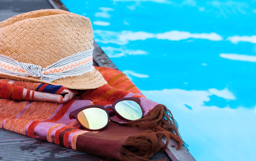 Vintage zomerrieten rieten strandmuts, zonnebril, omslagdoek bij zwembad, tropische achtergrond - Foto, afbeelding