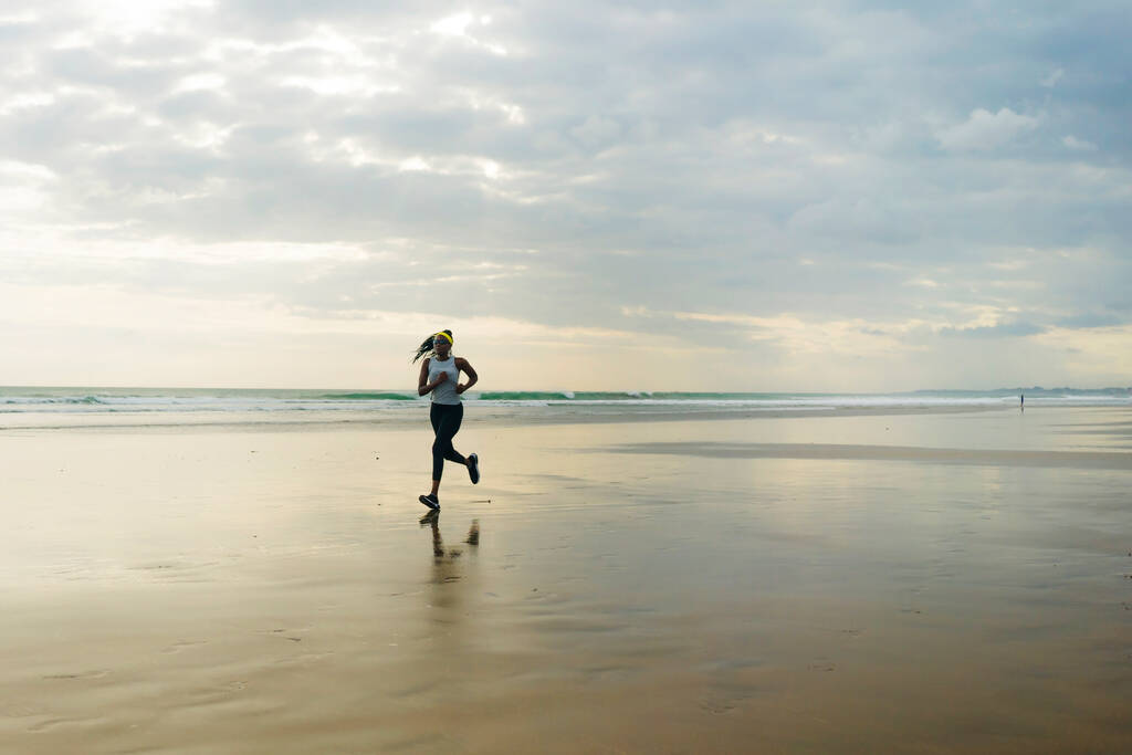 Silueta de mujer afroamericana corriendo en la playa - joven atractiva y atlética chica negra entrenando al aire libre haciendo ejercicio de jogging en el mar en forma física y estilo de vida saludable
 - Foto, Imagen