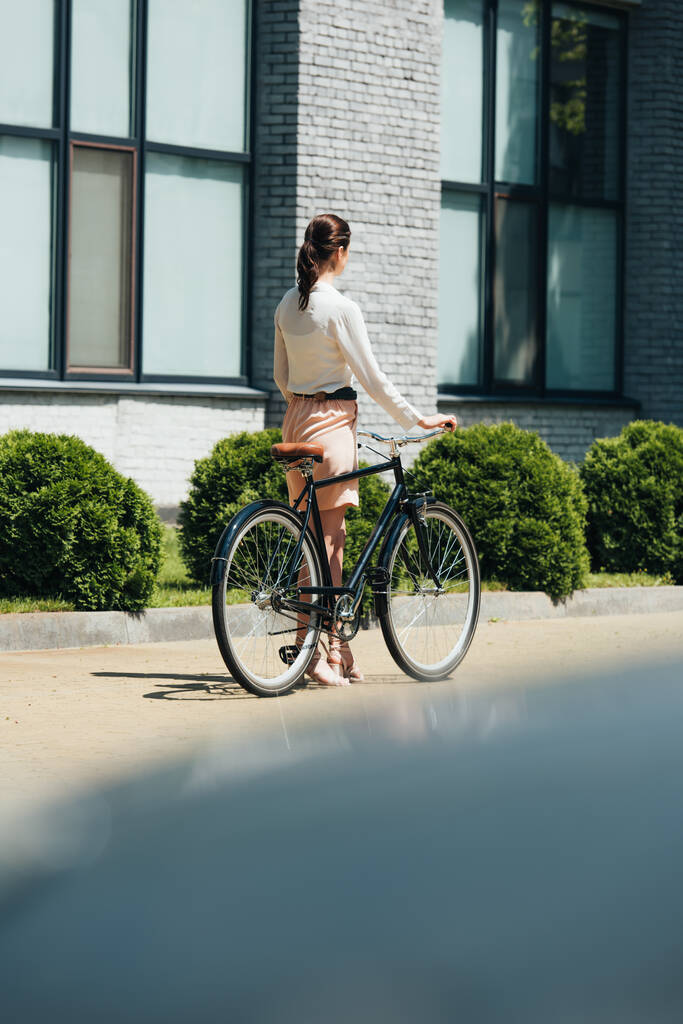 wybiórcze skupienie bizneswoman spaceru z rowerem w pobliżu nowoczesnego budynku  - Zdjęcie, obraz