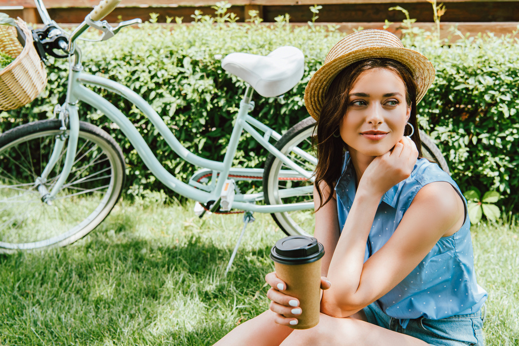 Tyttö olki hattu tilalla paperimuki ja istuu lähellä polkupyörää  - Valokuva, kuva