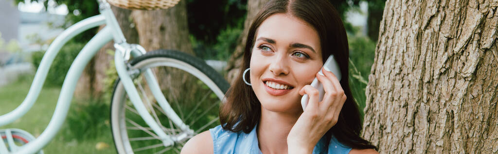 自転車の近くでスマートフォンで話している幸せな女性のパノラマ写真  - 写真・画像