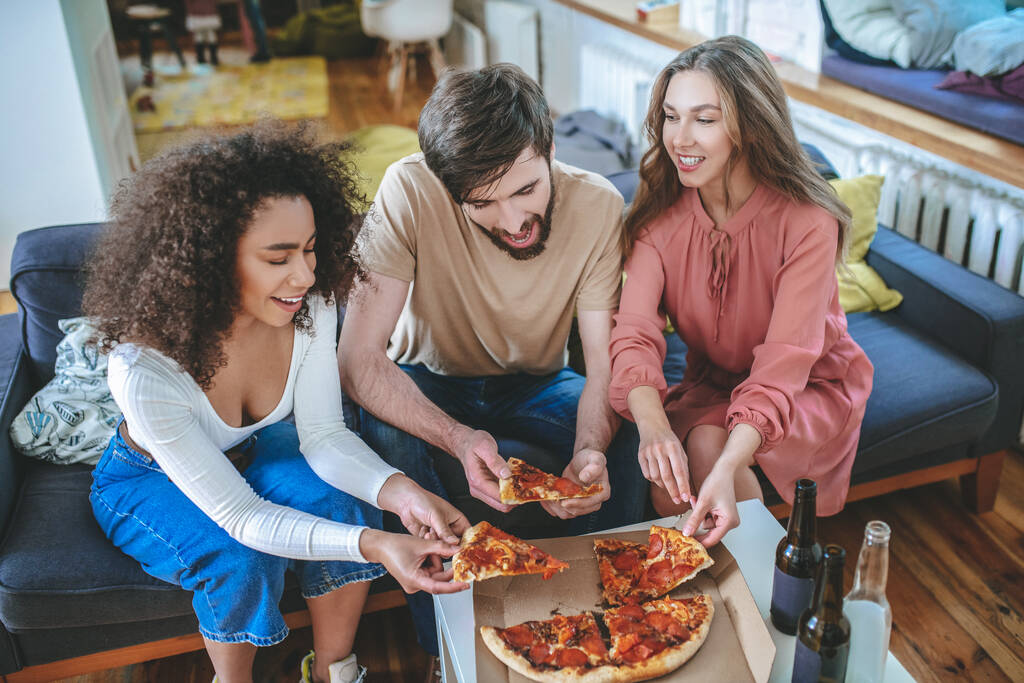 Trois jeunes amis sortant un morceau de pizza de la boîte - Photo, image