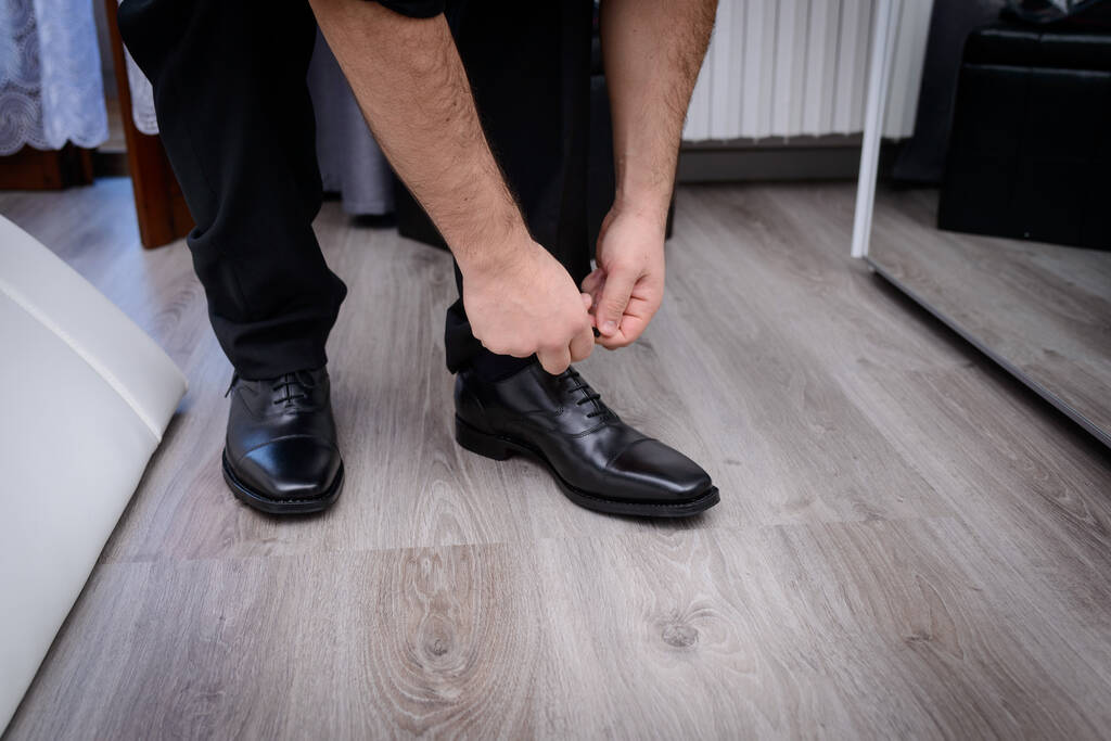 Gehakt schot van een man in zwart binden zijn schoenen in de voorkant van een spiegel - Foto, afbeelding
