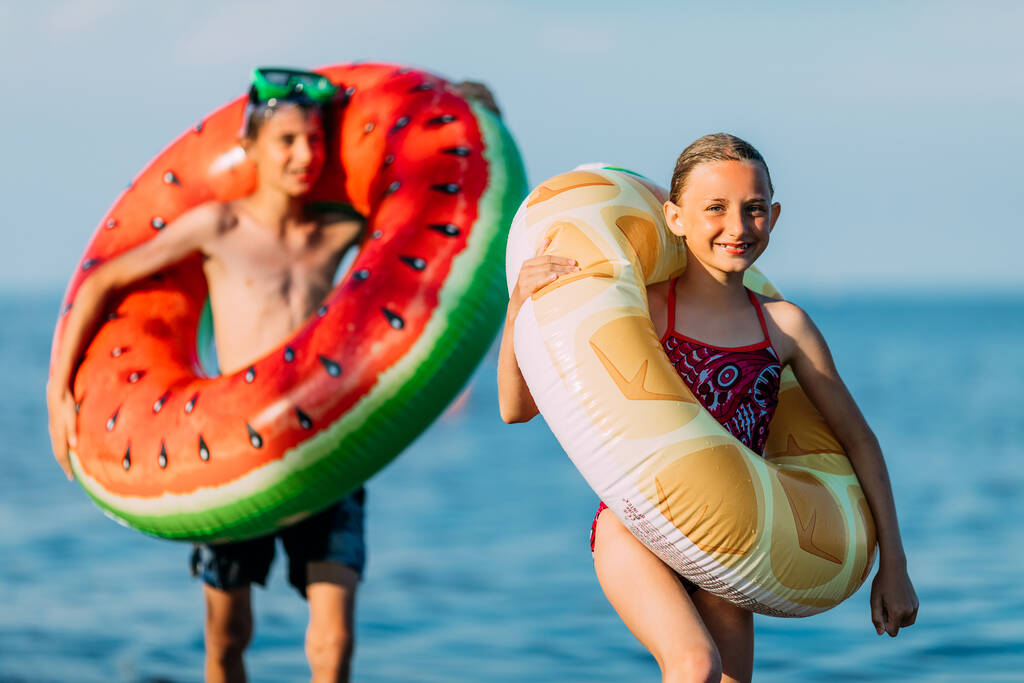 Mutlu çocuklar, erkek ve kız kardeşler şişirilebilir yüzme çemberleriyle sahilde eğleniyor. yaz tatili - Fotoğraf, Görsel