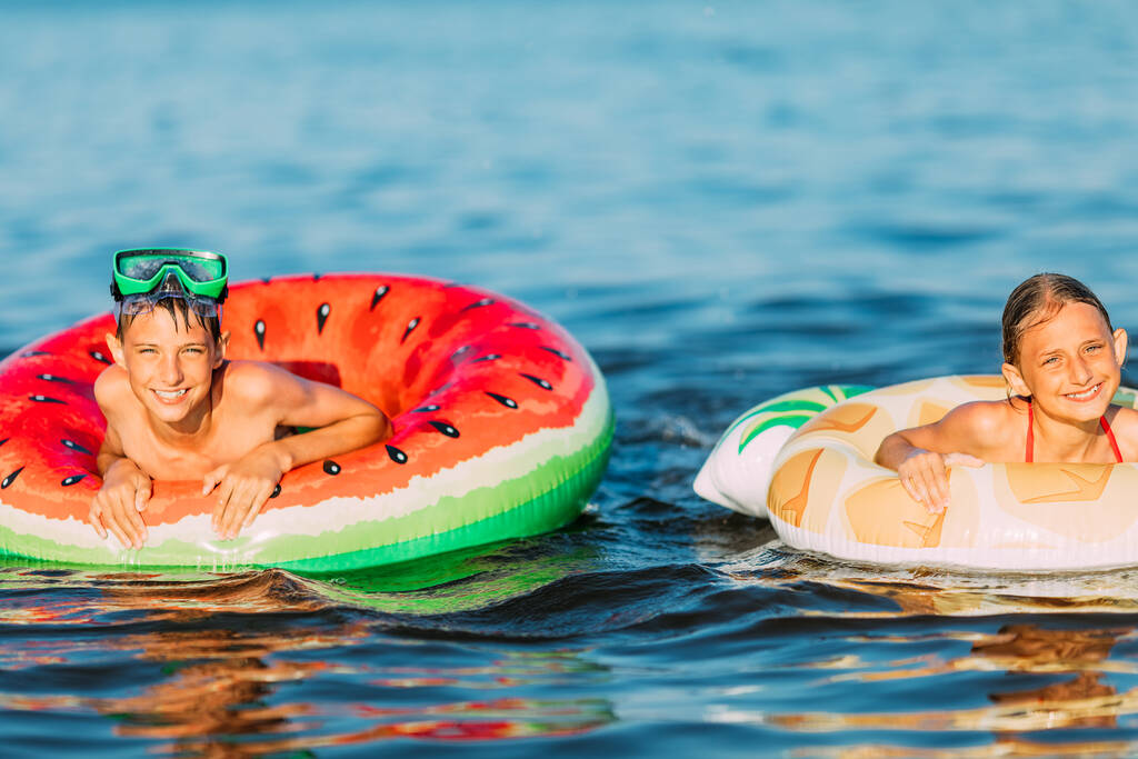 enfants garçon et fille, nager dans la mer avec des cercles gonflables, s'amuser sur la plage pendant les vacances d'été - Photo, image