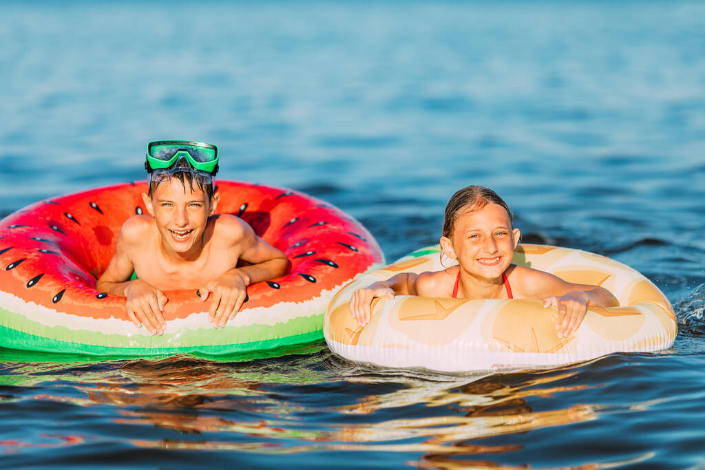 παιδιά αγόρι και κορίτσι, κολυμπούν στη θάλασσα με φουσκωτούς κύκλους, διασκεδάζοντας στην παραλία κατά τη διάρκεια των καλοκαιρινών διακοπών - Φωτογραφία, εικόνα