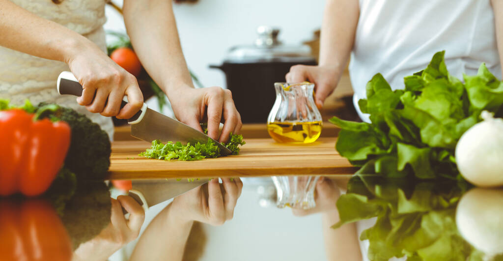 Nahaufnahme menschlicher Hände beim Kochen in der Küche. Mutter und Tochter oder zwei Freundinnen schneiden Gemüse für frischen Salat. Freundschaft, Familienessen und Lifestyle-Konzepte - Foto, Bild