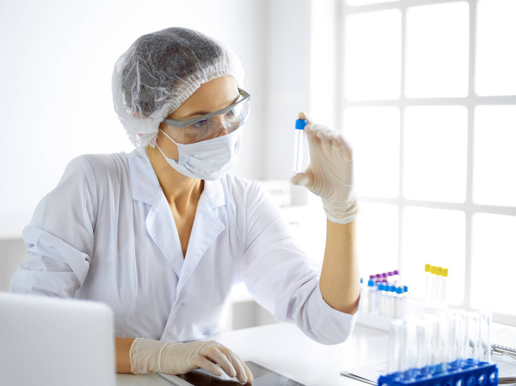 Professionele vrouwelijke wetenschapper in beschermende bril onderzoeken buis met reagentia in het laboratorium. Begrippen geneeskunde en onderzoek - Foto, afbeelding