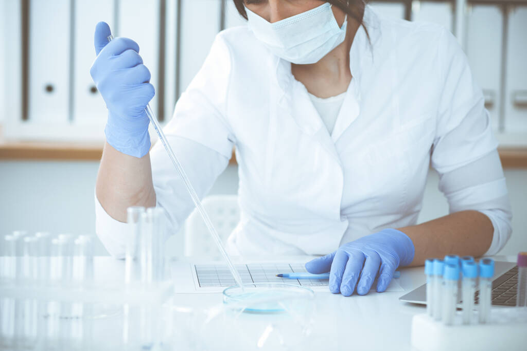 Κοντινό πλάνο της επαγγελματικής γυναίκας επιστήμονα σε προστατευτικά γυαλιά κάνοντας πείραμα με αντιδραστήρια στο εργαστήριο. Ιατρική και ερευνητική έννοια - Φωτογραφία, εικόνα