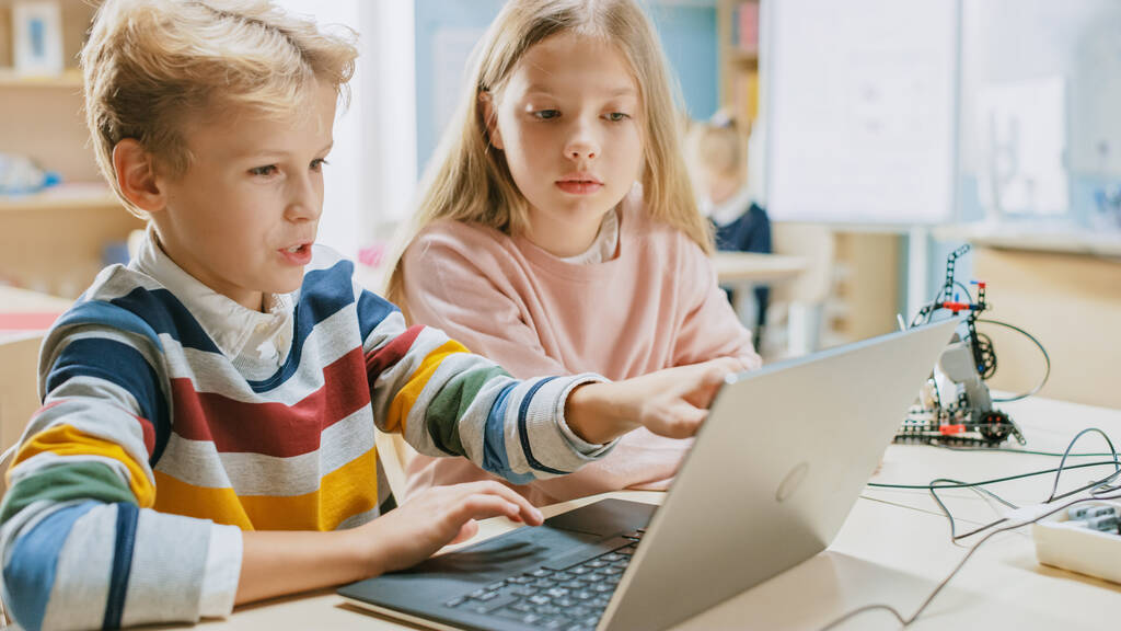 Brilliant Schoolgirl και Schoolboy Talk and Use Laptop to Program Software for Robotics Engineering Class. Δημοτικό Σχολείο Science Classroom με τα παιδιά που εργάζονται στην τεχνολογία. STEM Εκπαίδευση - Φωτογραφία, εικόνα