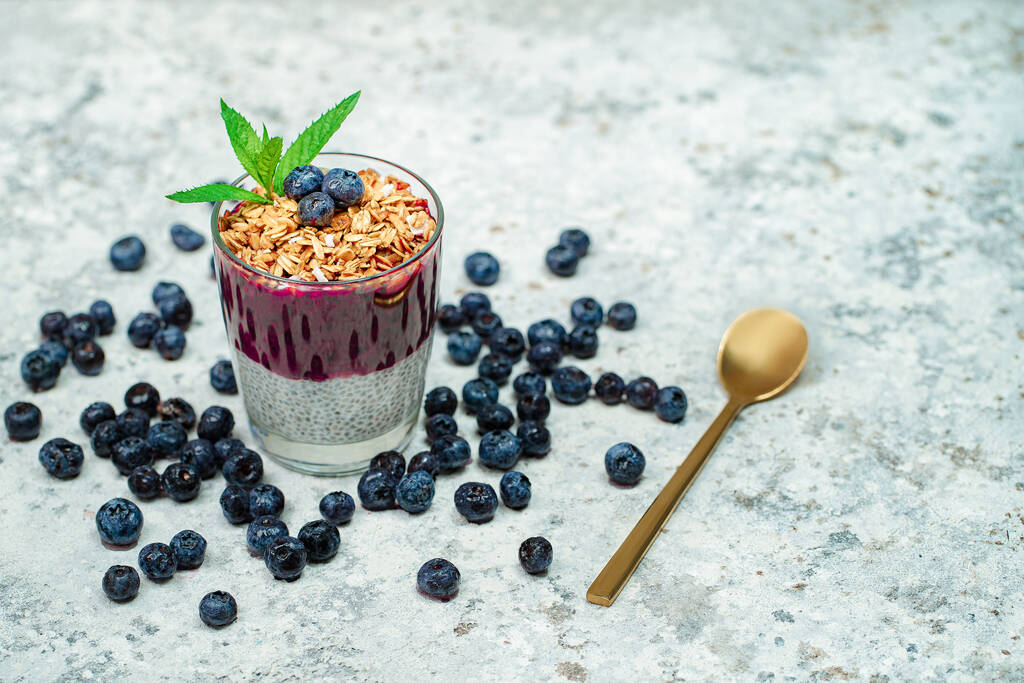 Healthy breakfast or morning snack with chia seeds pudding, granola, muesli and blueberries on white stone background, vegetarian food, diet and health concept - Photo, Image