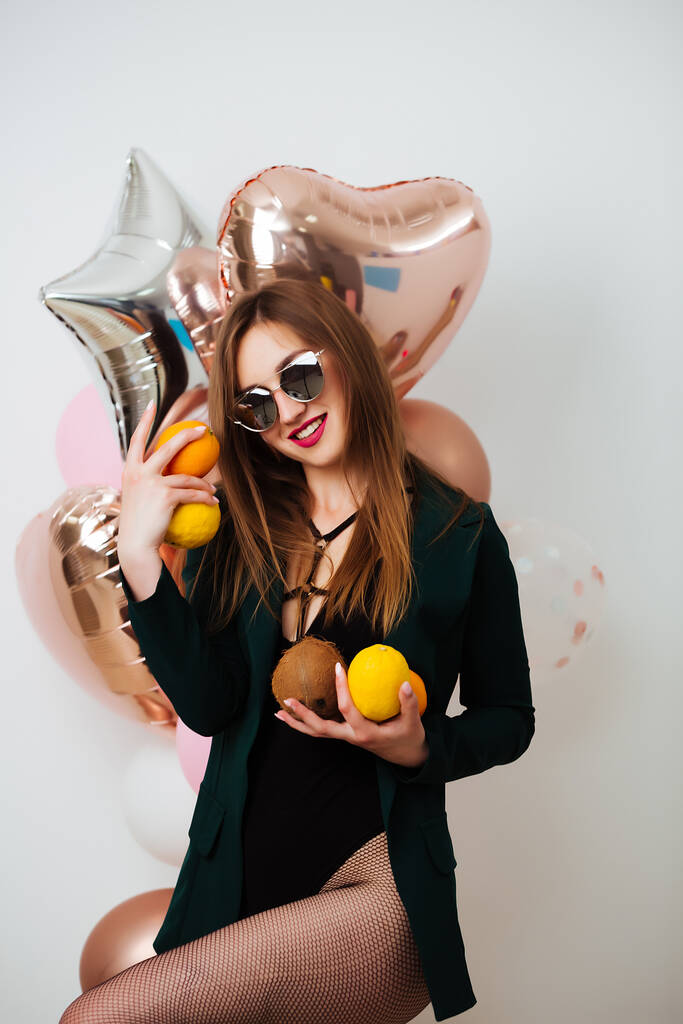 Стройная девушка в телесном костюме и цветные шарики в руках стоят на коричневом фоне в праздничном настроении, позируя перед камерой
. - Фото, изображение
