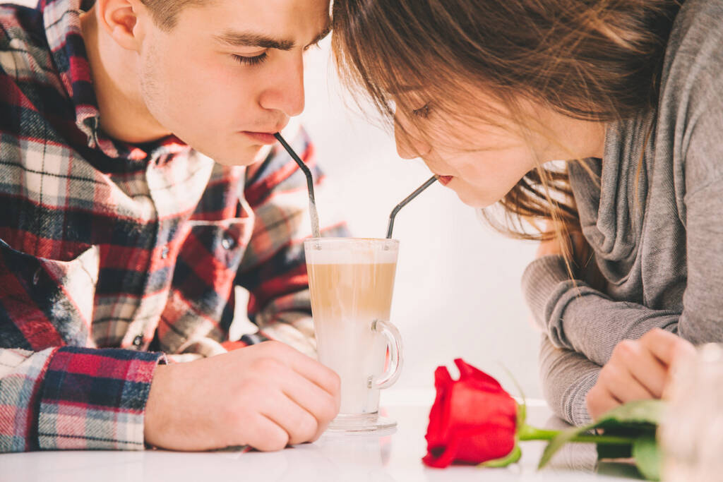 Zakochana kobieta i mężczyzna pijący latte ze słomkami z tej samej szklanki, spędzający wolny czas razem. - Zdjęcie, obraz