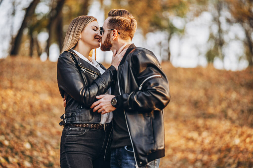 Beau jeune couple marchant dans le parc d'automne par une journée ensoleillée. Ils s'embrassent et sourient, profitent d'une promenade. - Photo, image