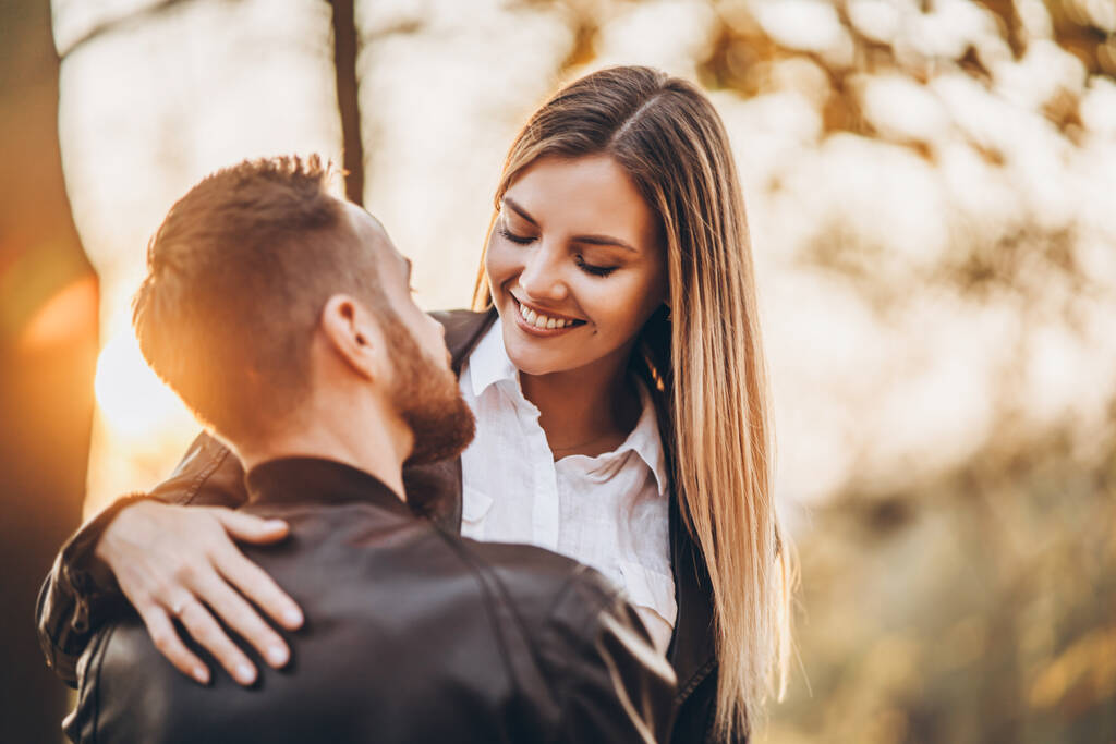 Nuori pari suutelee taustalla syksyn puistossa. Mies nosti naisen syliinsä.. - Valokuva, kuva