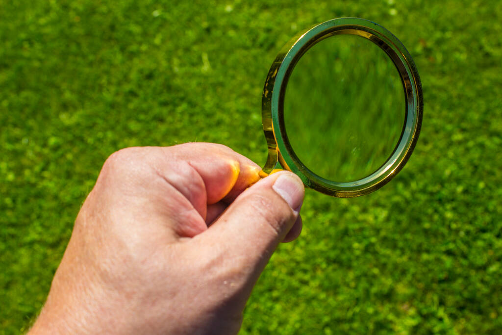 Uma lupa com uma lente em uma moldura de metal amarelo na mão do homem
 - Foto, Imagem