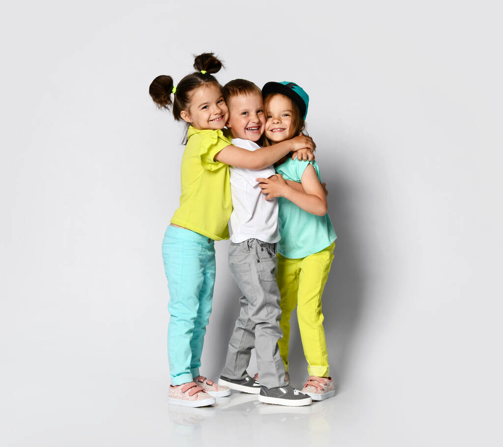 Studio portrét dětí na světlém pozadí: celotělový záběr tří dětí v jasném oblečení, dvou dívek a jednoho chlapce.  - Fotografie, Obrázek