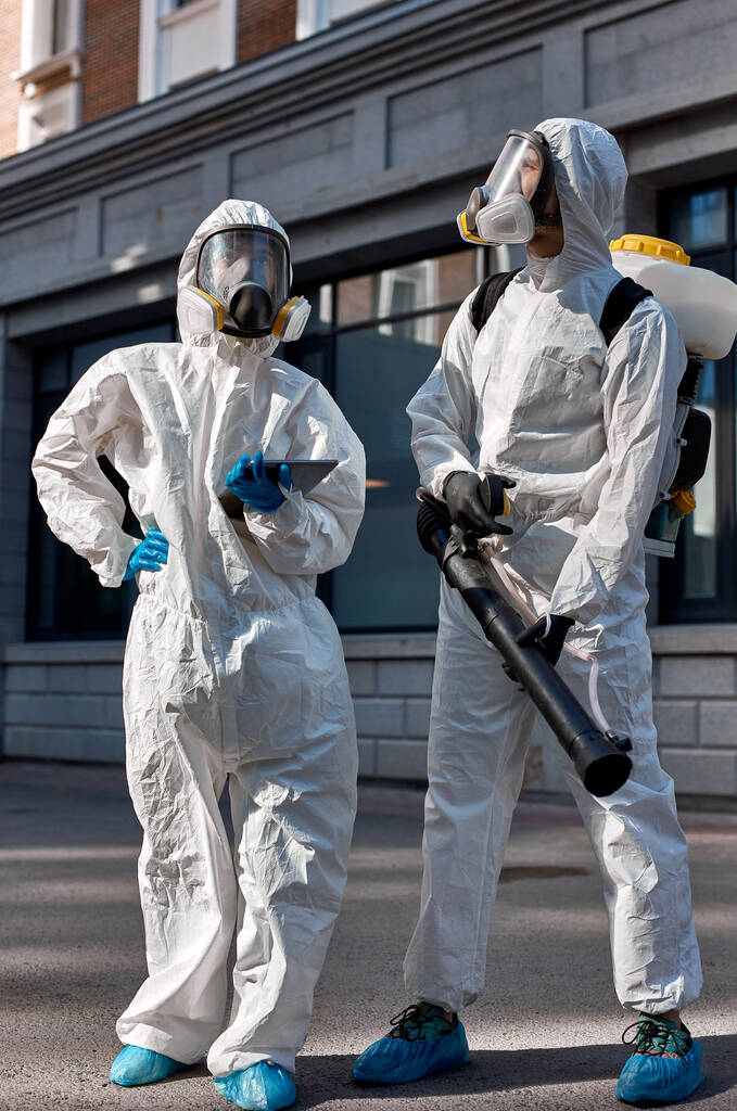 Profesjonalne dezynfektory w ochronnym kombinezonie ochronnym spacerujące ulicami miasta - Zdjęcie, obraz