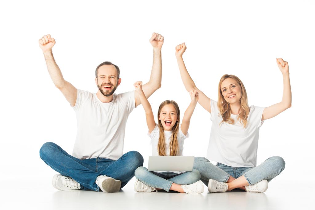 excited parents sitting on floor near happy daughter with laptop isolated on white - Photo, Image