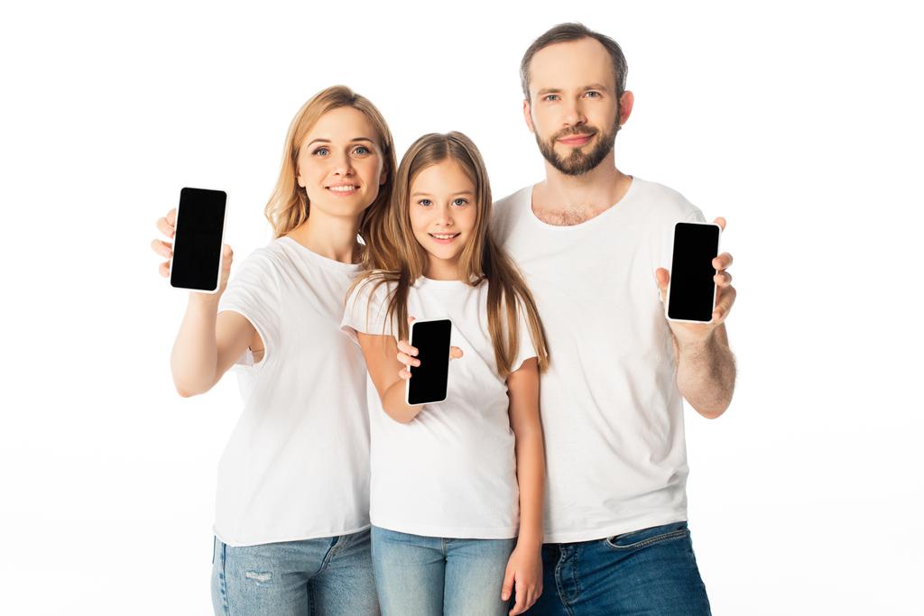 hymyilevä perhe valkoisissa t-paidoissa, joissa näkyy valkoisella eristetyt tyhjät ruudut älypuhelimissa - Valokuva, kuva