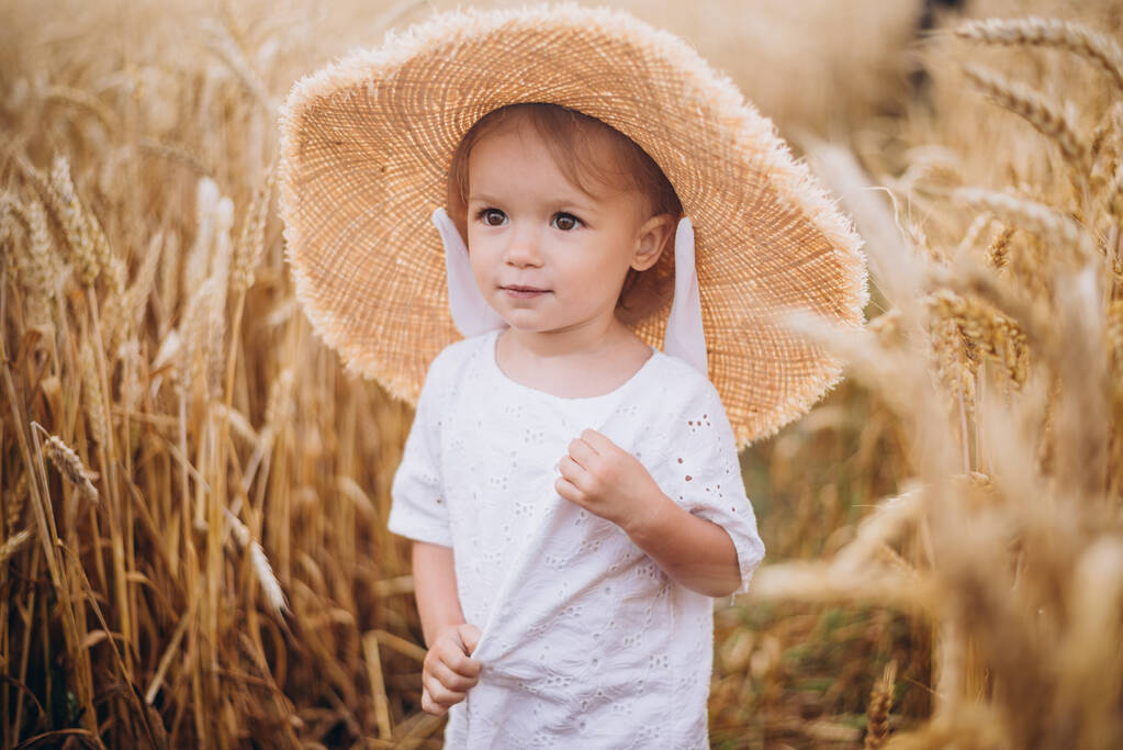 vrij schattig baby meisje met een mooie glimlach dragen zomer stro hoed in een wandeling in de tarwevelden. selectieve focus. familie, mensen concept - Foto, afbeelding