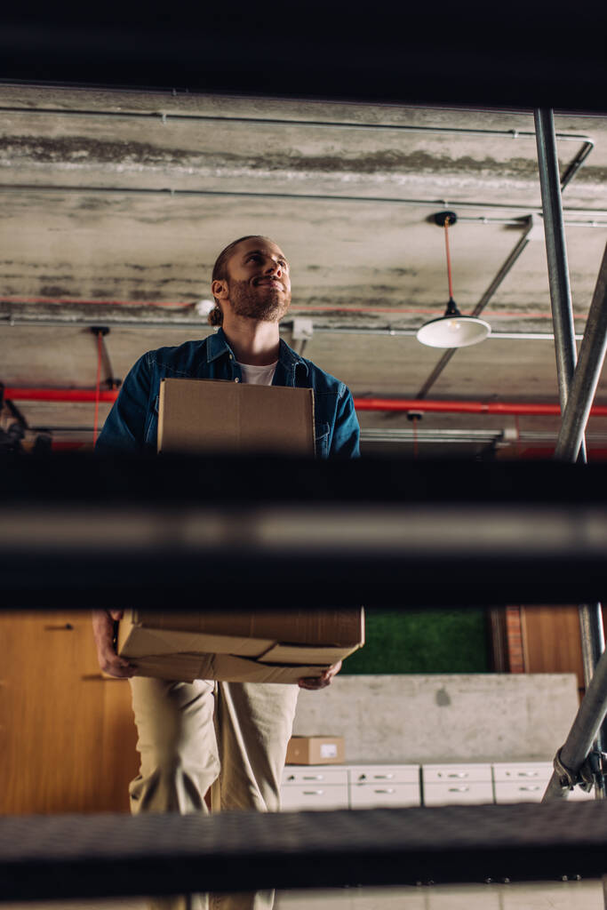 enfoque selectivo de empresario feliz sosteniendo cajas mientras camina por las escaleras en la oficina
 - Foto, Imagen