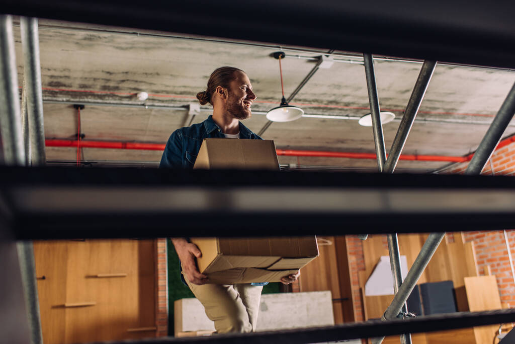 избирательный фокус жизнерадостного бизнесмена, держащего коробки во время прогулки по лестнице в офисе
 - Фото, изображение