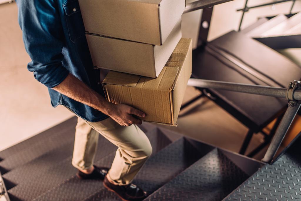 visão parcial do empresário segurando caixas de papelão e andando em escadas no escritório
 - Foto, Imagem