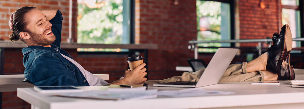панорамний урожай веселого бізнесмена тримає паперовий стаканчик і дивиться на ноутбук в офісі
 - Фото, зображення