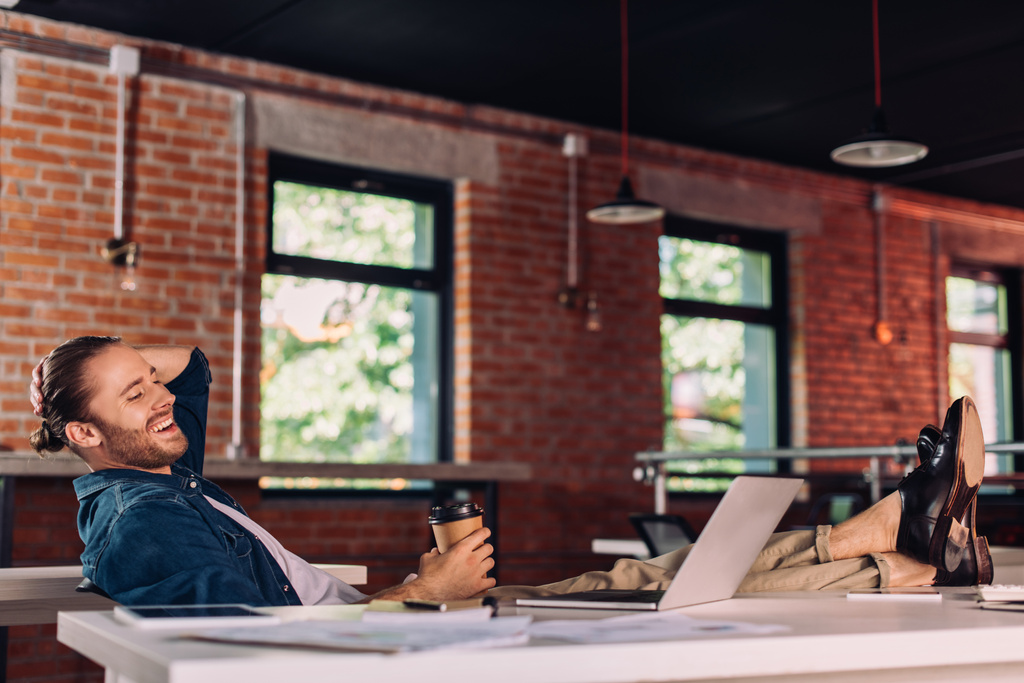 вибірковий фокус веселого бізнесмена тримає паперовий стаканчик і дивиться на ноутбук в офісі
 - Фото, зображення