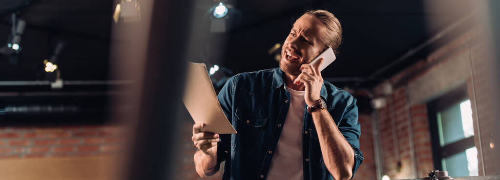 concept horizontal d'homme d'affaires émotionnel parlant sur smartphone et tenant dossier dans le bureau - Photo, image