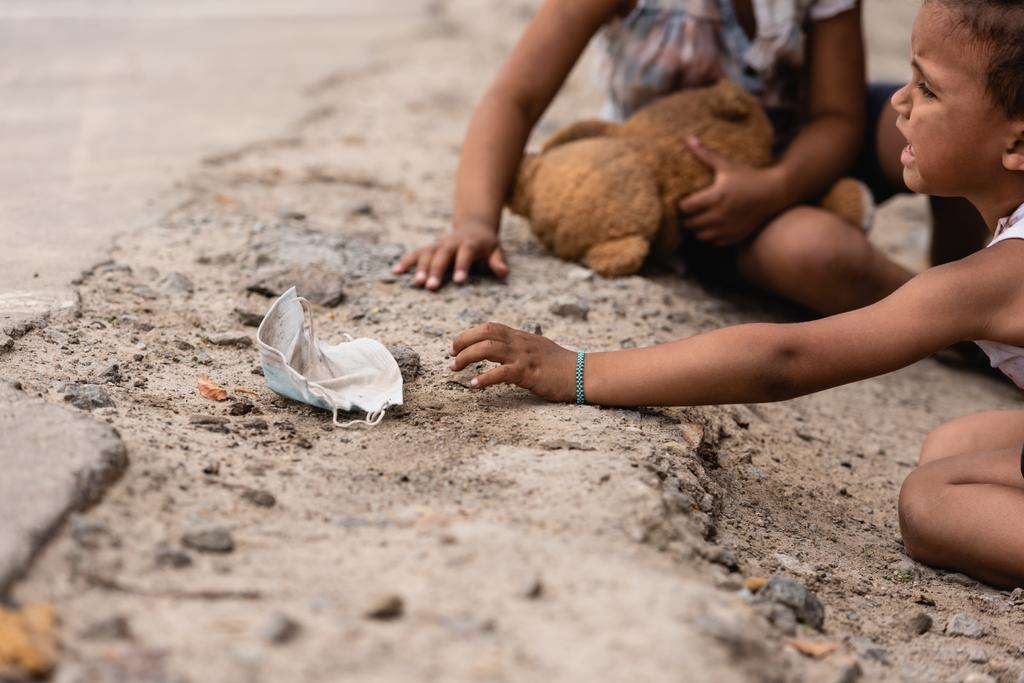 foco seletivo do pobre menino afro-americano chorando enquanto alcança máscara médica suja perto da irmã no chão
 - Foto, Imagem