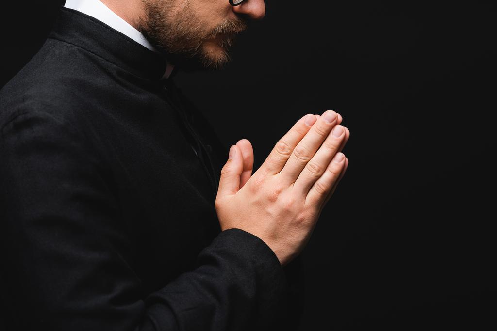 částečný pohled na kněze s modlícími se rukama izolovanými na černém  - Fotografie, Obrázek