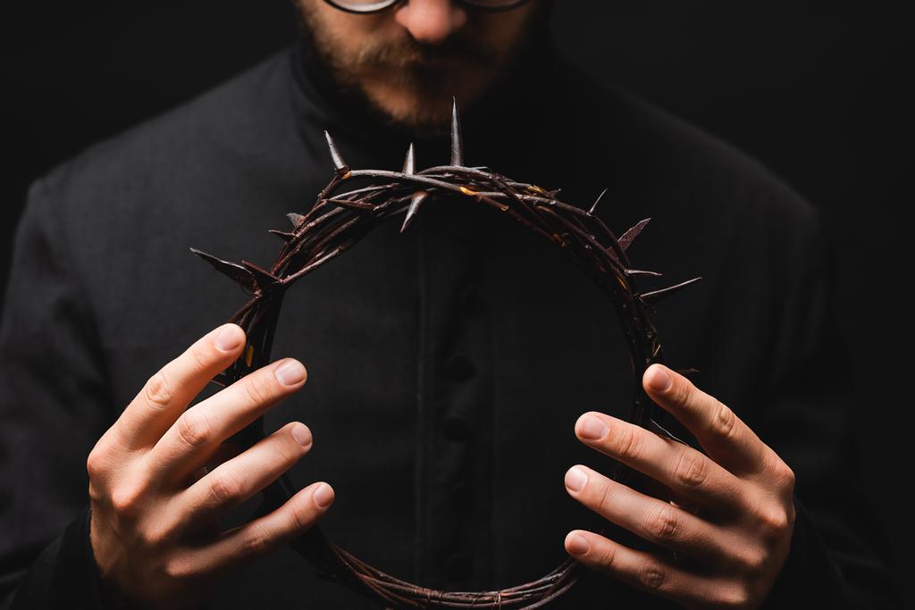 selectieve focus van priester houden krans met spikes in handen geïsoleerd op zwart  - Foto, afbeelding