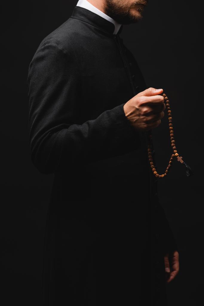 abgeschnittene Ansicht des Priesters, der Rosenkranzperlen hält und isoliert auf schwarz steht  - Foto, Bild