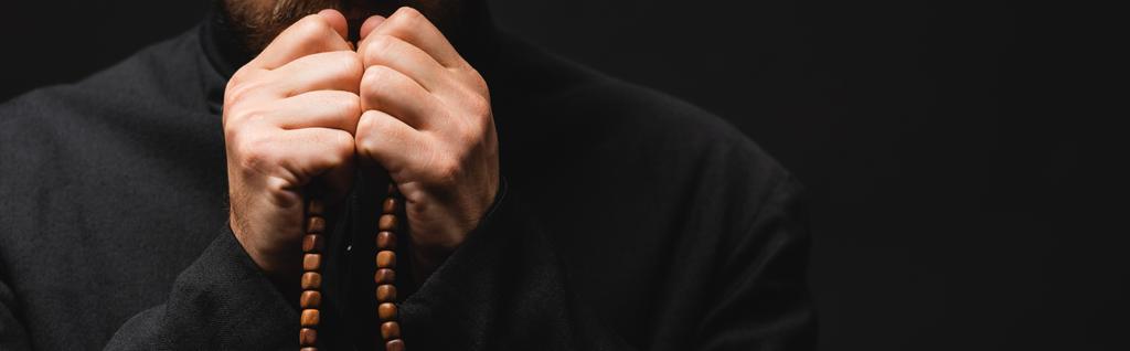 cultivo panorámico de sacerdote sosteniendo cuentas de rosario en manos aisladas en negro
  - Foto, Imagen