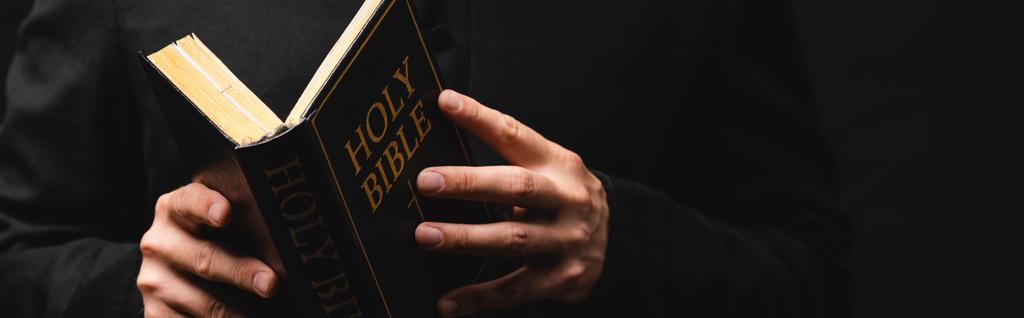 vodorovný obraz pastora, jak čte Bibli svatou izolovanou na černém  - Fotografie, Obrázek