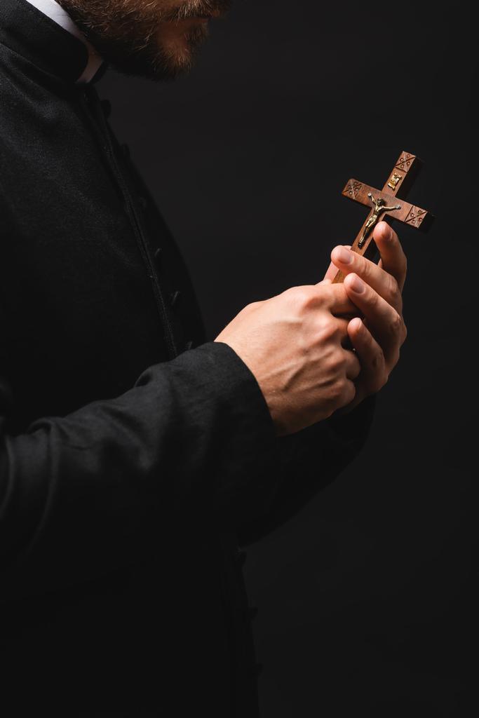 vista recortada del sacerdote sosteniendo cruz de madera aislada en negro
  - Foto, imagen
