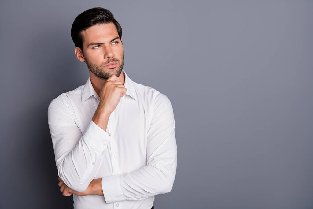 Zdjęcie młodego biznesmena mężczyzna pracodawca trzymać rękę na podbródku wygląd ciekawy puste miejsce nie uśmiechając się myśleć o startup smart person nosić białą koszulę biurową odizolowany szary kolor tła - Zdjęcie, obraz