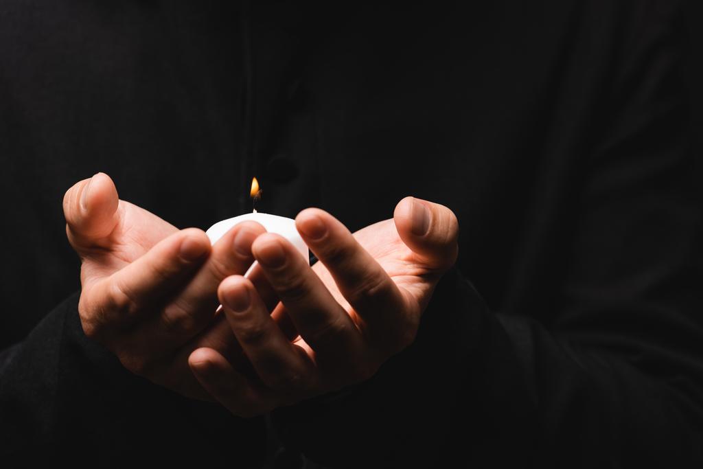 partial view of priest holding burning candle isolated on black  - Photo, Image