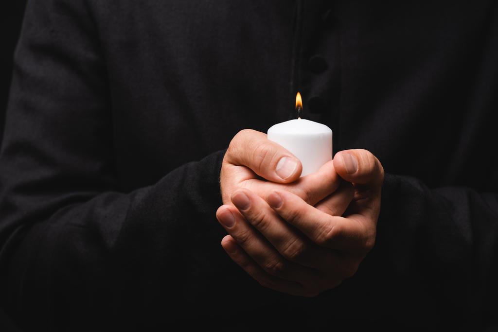 vista recortada del sacerdote sosteniendo vela encendida en las manos aisladas en negro
  - Foto, Imagen